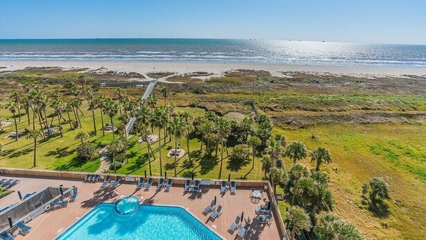 A resort with a swimming pool, lounge chairs, and a view of the beach and ocean.