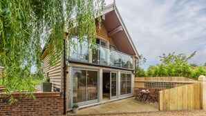 Ein zweistöckiges Haus mit Balkon, Terrasse und Gartenmöbeln sowie einem Holzzaun.