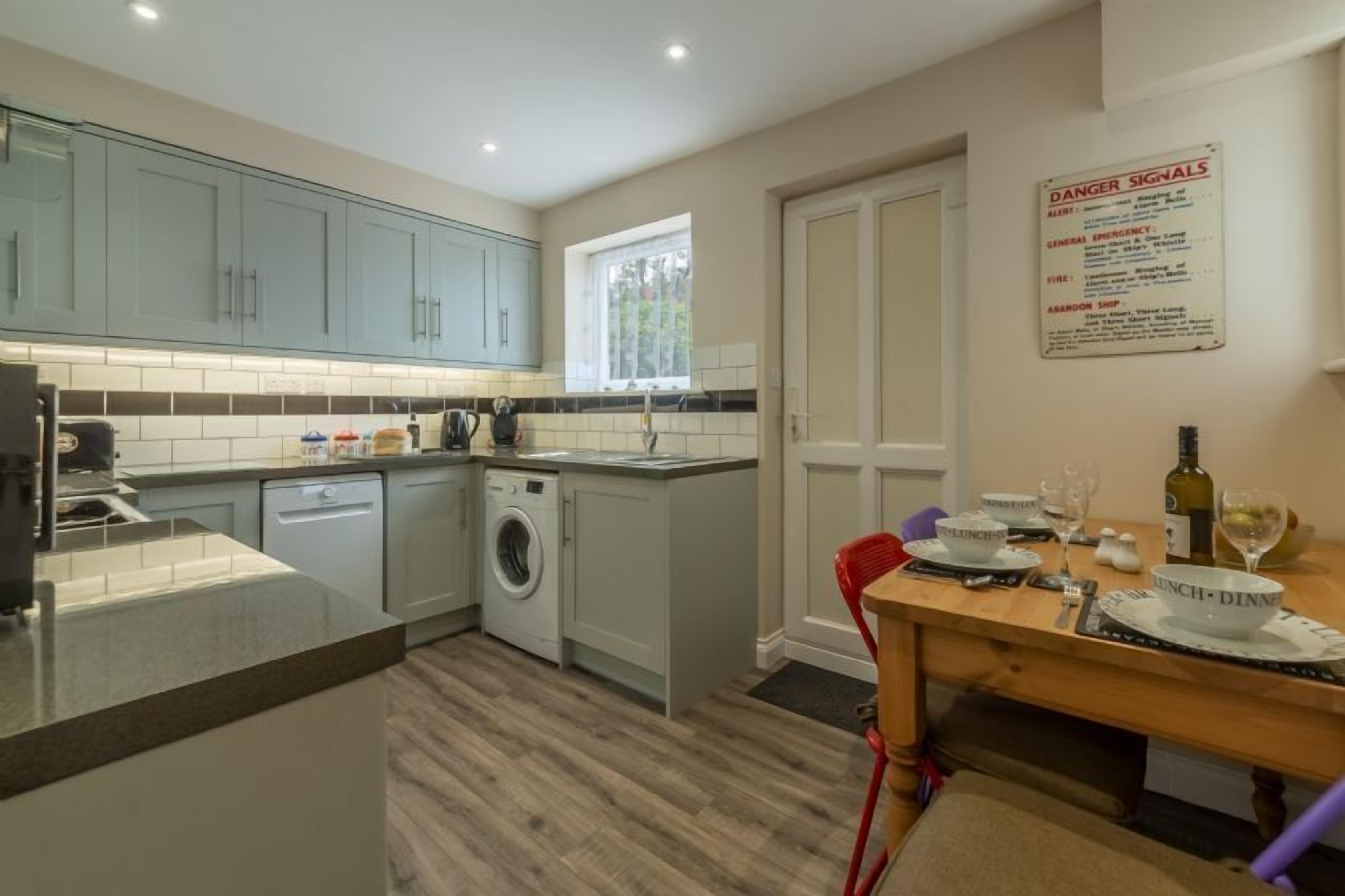 Une cuisine compacte avec des meubles de couleur bleu clair, un lave-linge et un coin repas avec une table dressée pour deux personnes.