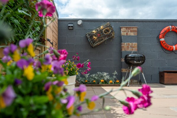 A garden area with a barbecue grill, a brick wall, and a lifebuoy.