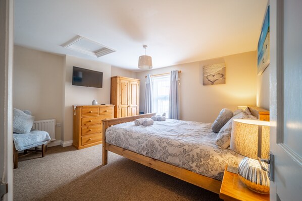 A bedroom with a wooden bed, a dresser, a television, and a window with curtains. - Seaside Cottage, Wells-next-the-Sea, Norfolk (Wells-next-the-Sea)