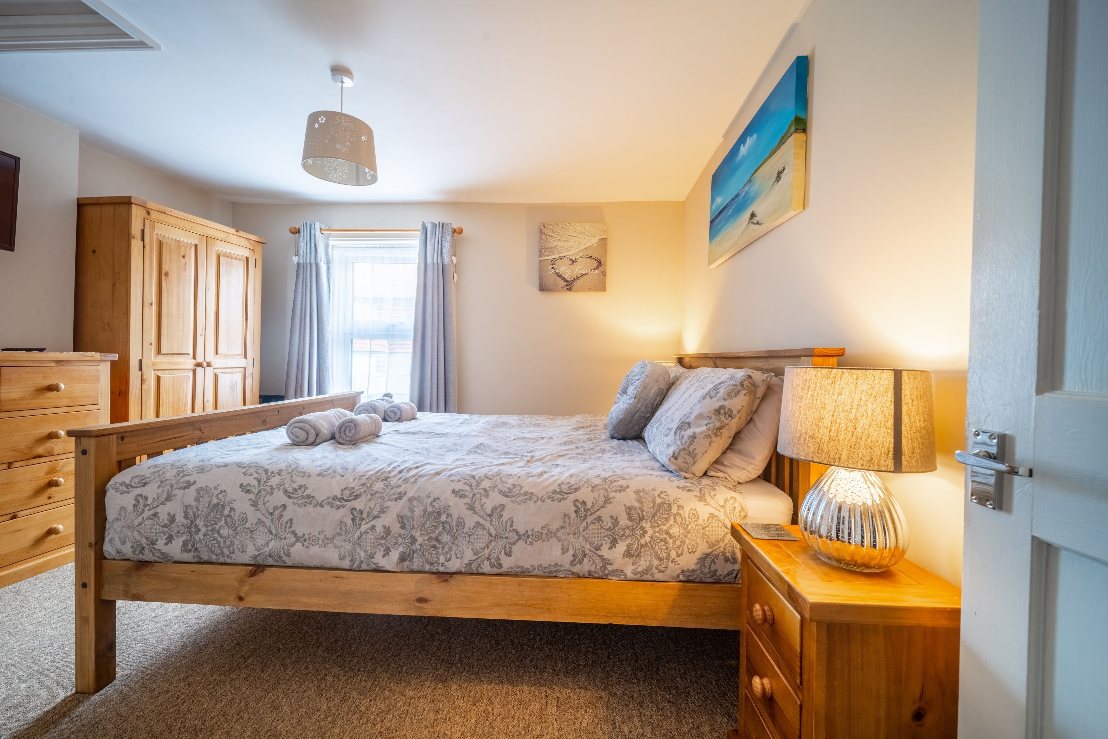 Een slaapkamer met een houten bed, een nachtkastje met een lamp, een kledingkast en een schilderij aan de muur.
