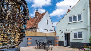 A patio with a table and chairs, a white house with a red-tiled roof, and a blue fence. - Seaside Cottage, Wells-next-the-Sea, Norfolk (Wells-next-the-Sea)