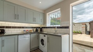 A compact kitchen with grey cabinets, a dishwasher, a washing machine, and a window with a view of the outside. - Seaside Cottage, Wells-next-the-Sea, Norfolk (Wells-next-the-Sea)