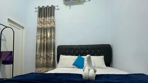 Cama bem arrumada com manta azul, travesseiro branco e almofada decorativa azul.