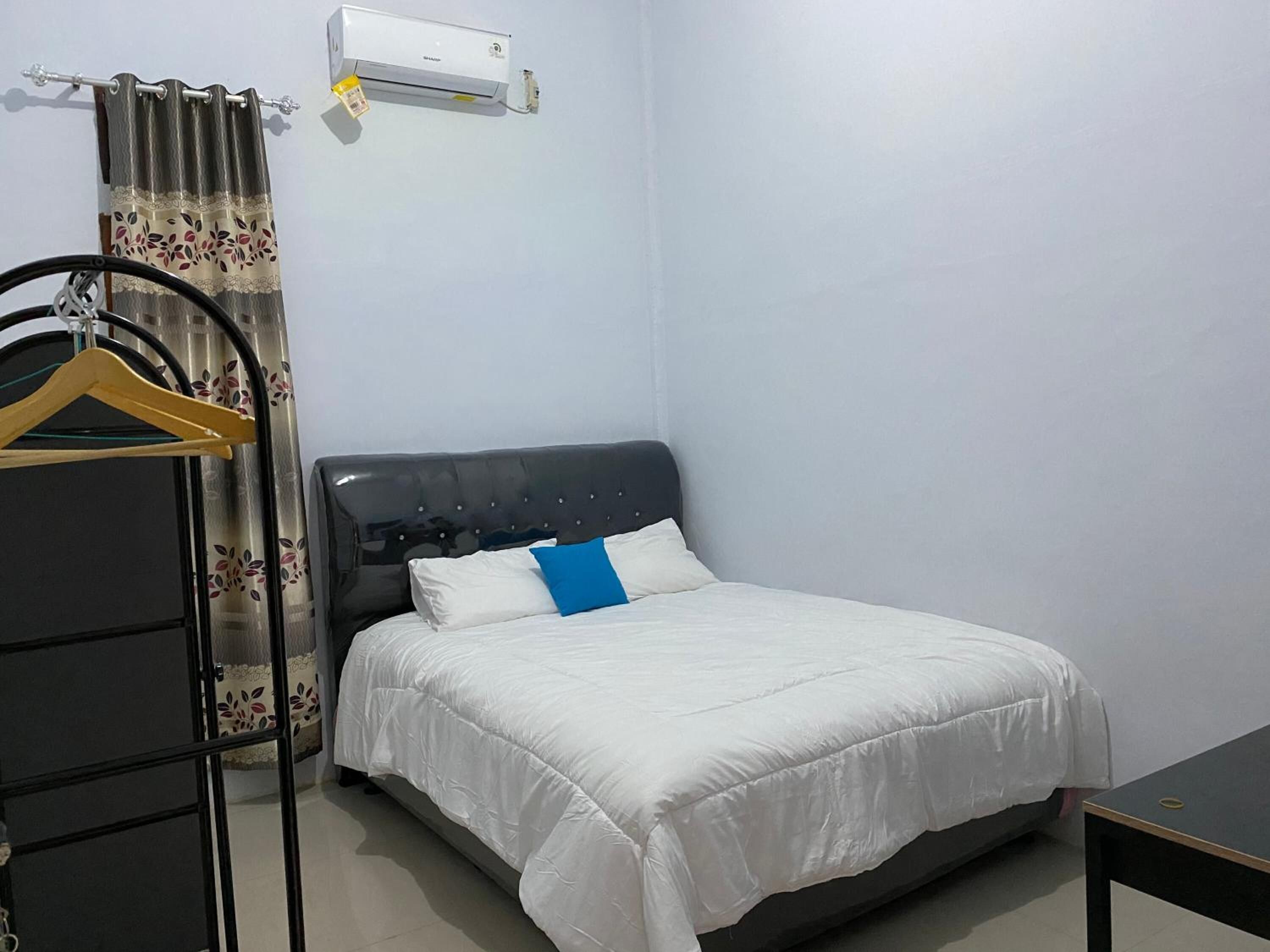 Un dormitorio con cama, perchero, cortina y unidad de aire acondicionado.