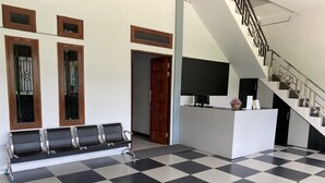 Uma área de recepção com piso xadrez, um banco e um balcão de atendimento com televisão de tela plana.