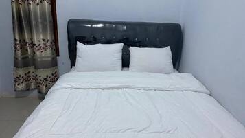 Een bed met een donker hoofdbord en witte beddengoed in een kamer met lichtgekleurde muren en een bloemen gordijn.