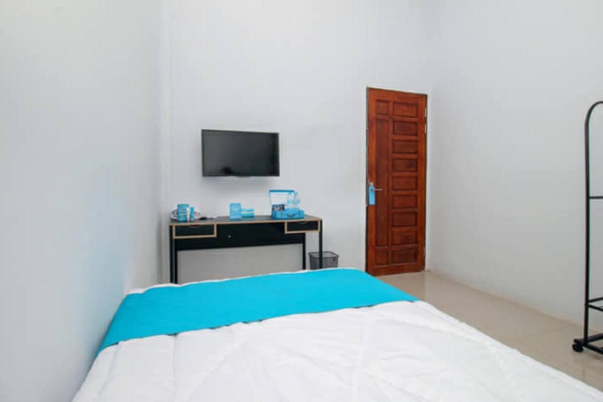 Een slaapkamer met een bed, een bureau met een televisie, en een deur.