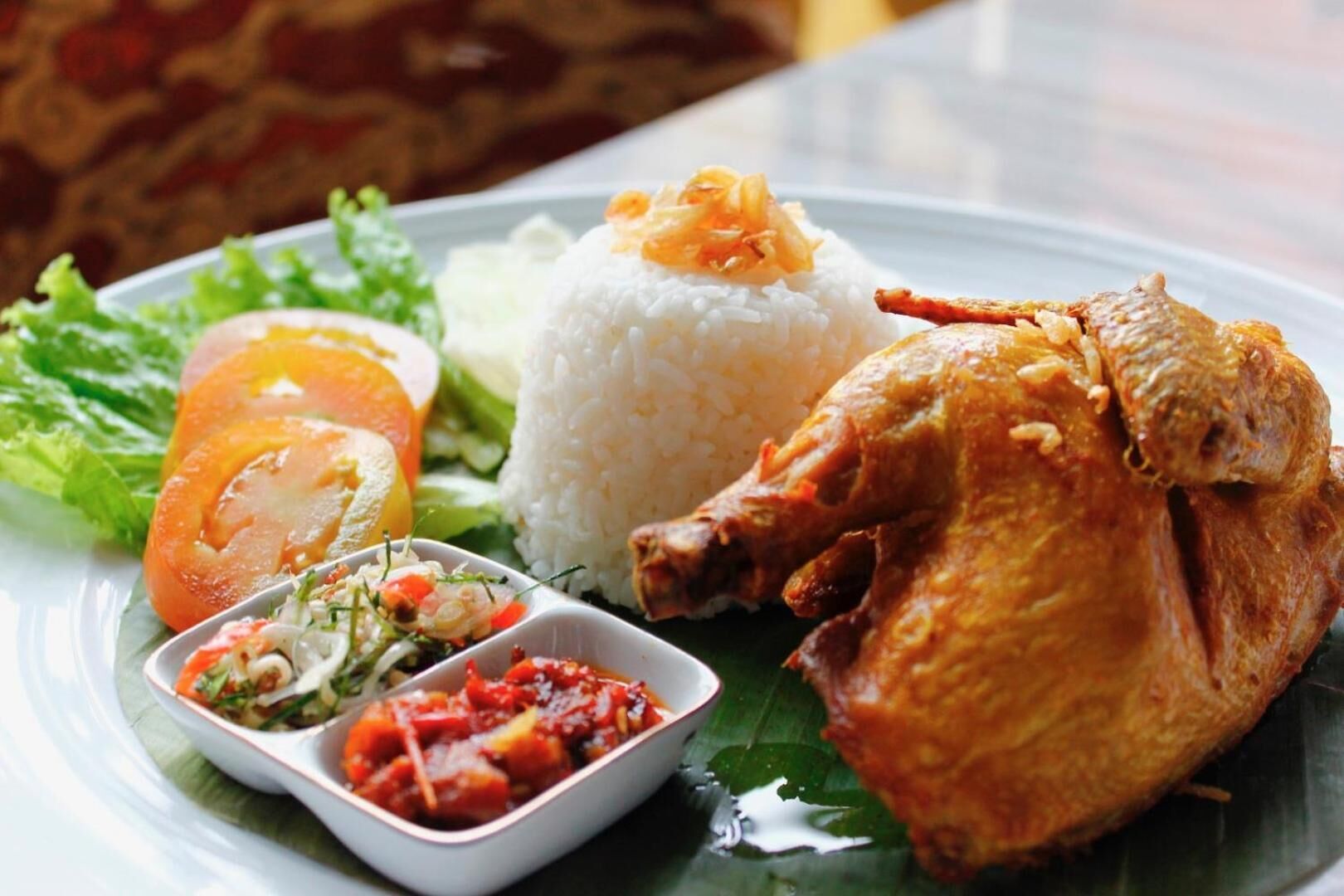 A plate with rice, a roasted chicken, a salad, and a small bowl of sauce.