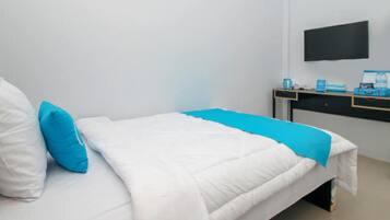 Un lit bien fait, avec une literie blanche et bleue, un téléviseur noir fixé au mur et un bureau sur lequel se trouvent un ordinateur et quelques objets.