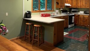 A kitchen with wooden cabinets, a large window with a view of trees, a stove, and a sink.
