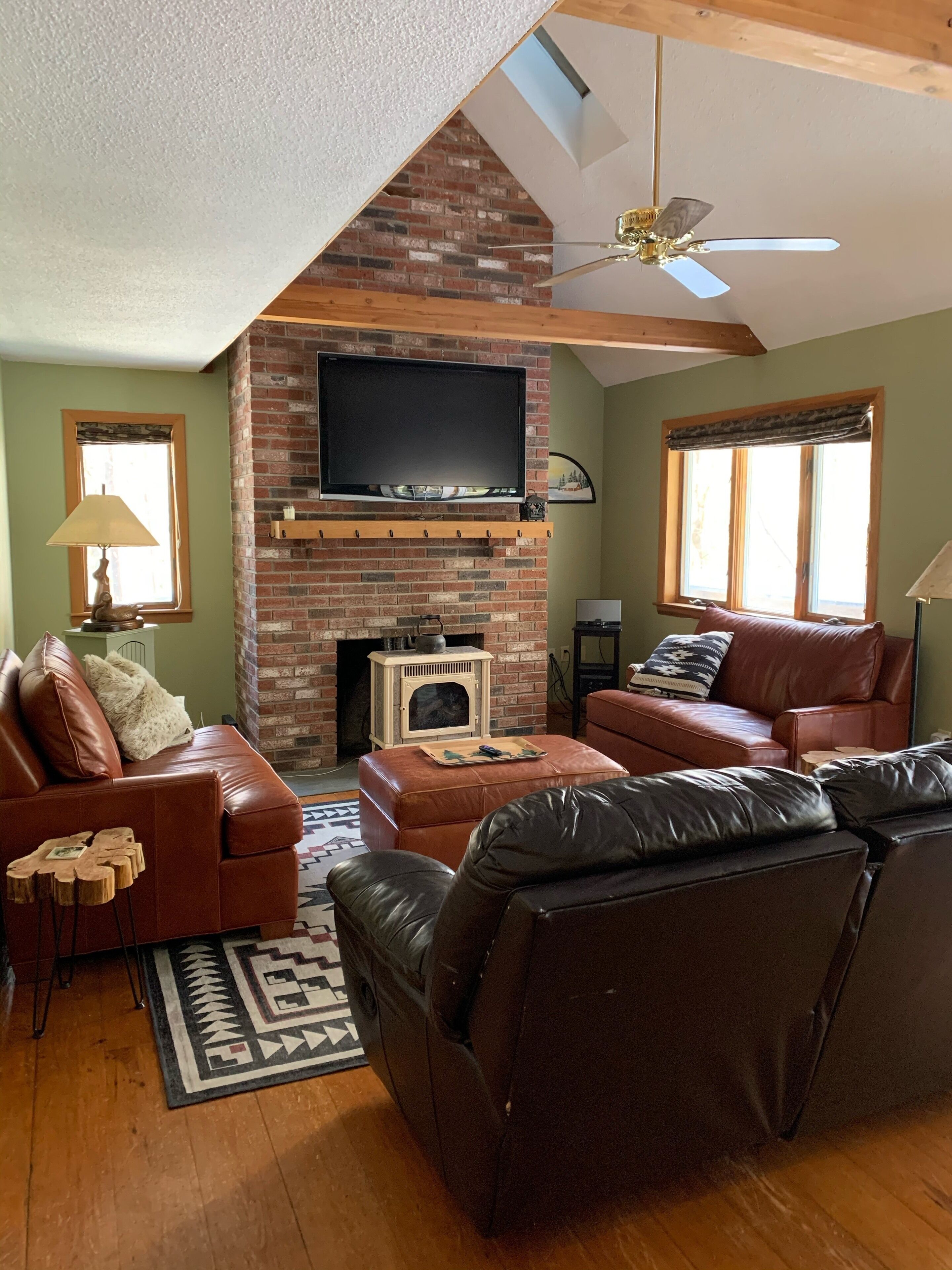 Una sala de estar acogedora con chimenea de ladrillo, sofás de cuero, televisor de pantalla plana y ventilador de techo.