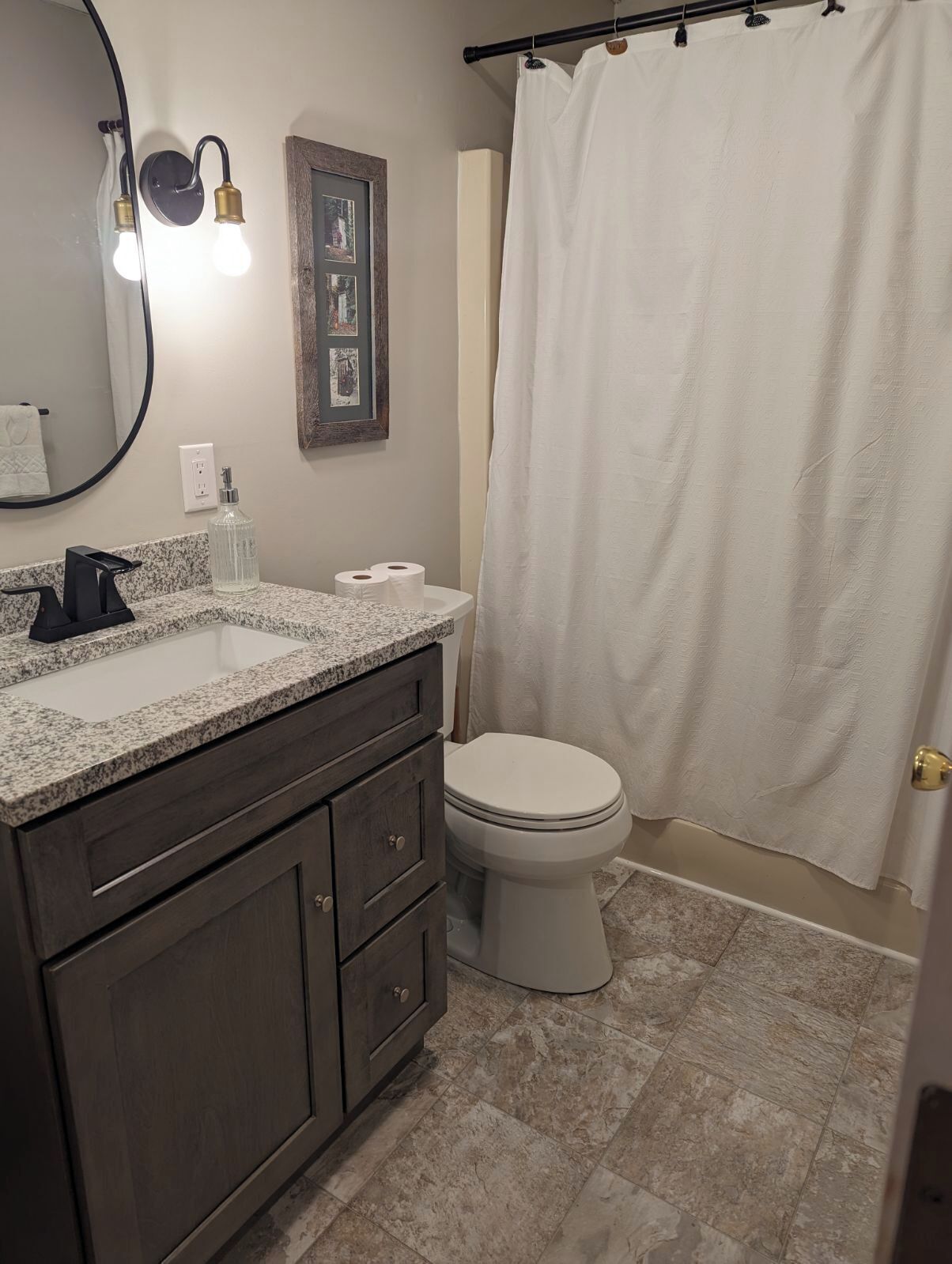 A bathroom with a granite countertop sink, dark wooden cabinets, a white toilet, and a shower curtain.