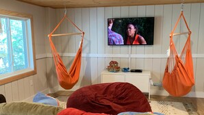 A room with a sofa, two hanging hammocks, a television, and a window.