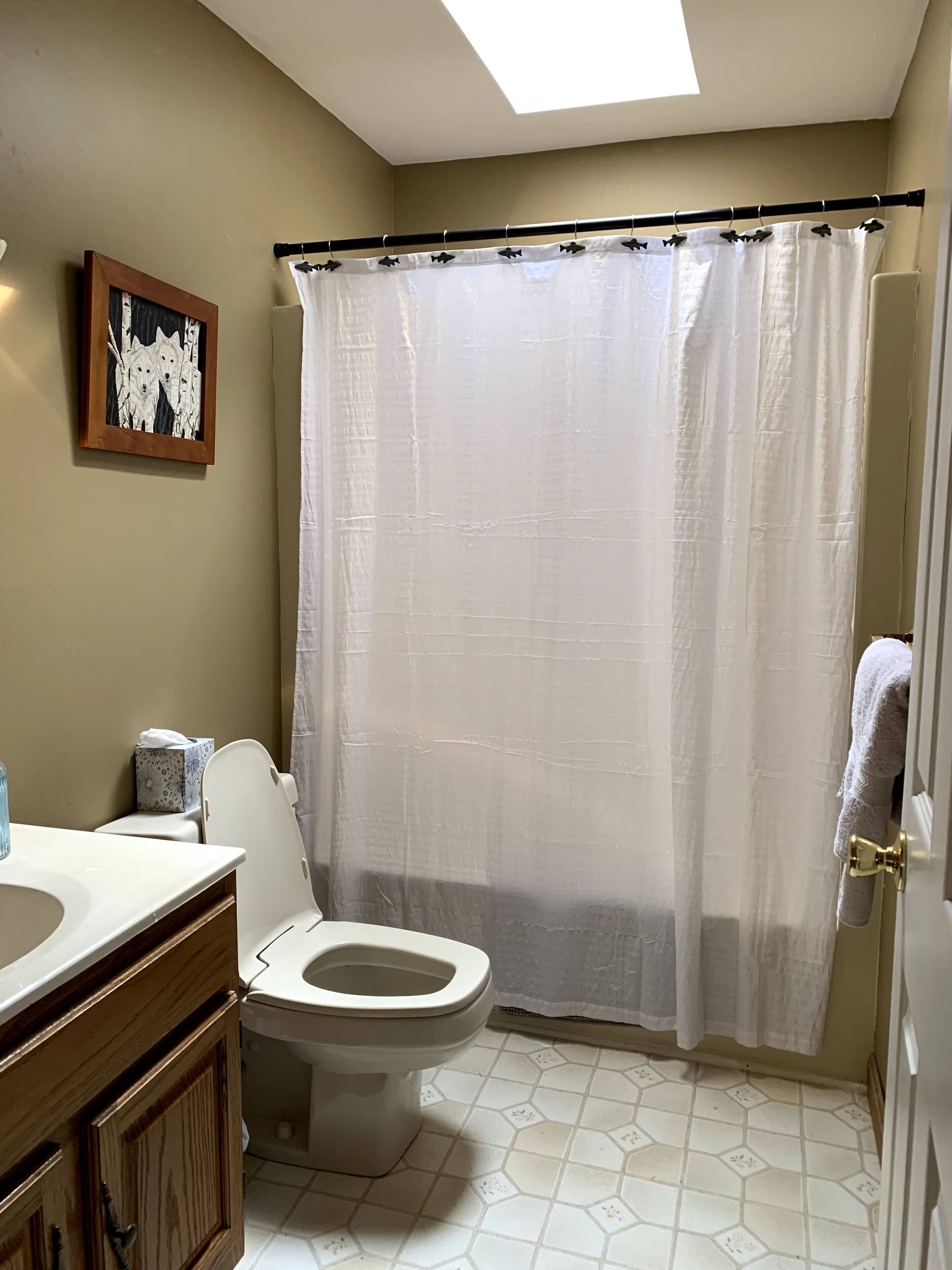 A bathroom with a toilet, a sink, a framed picture on the wall, and a shower curtain.