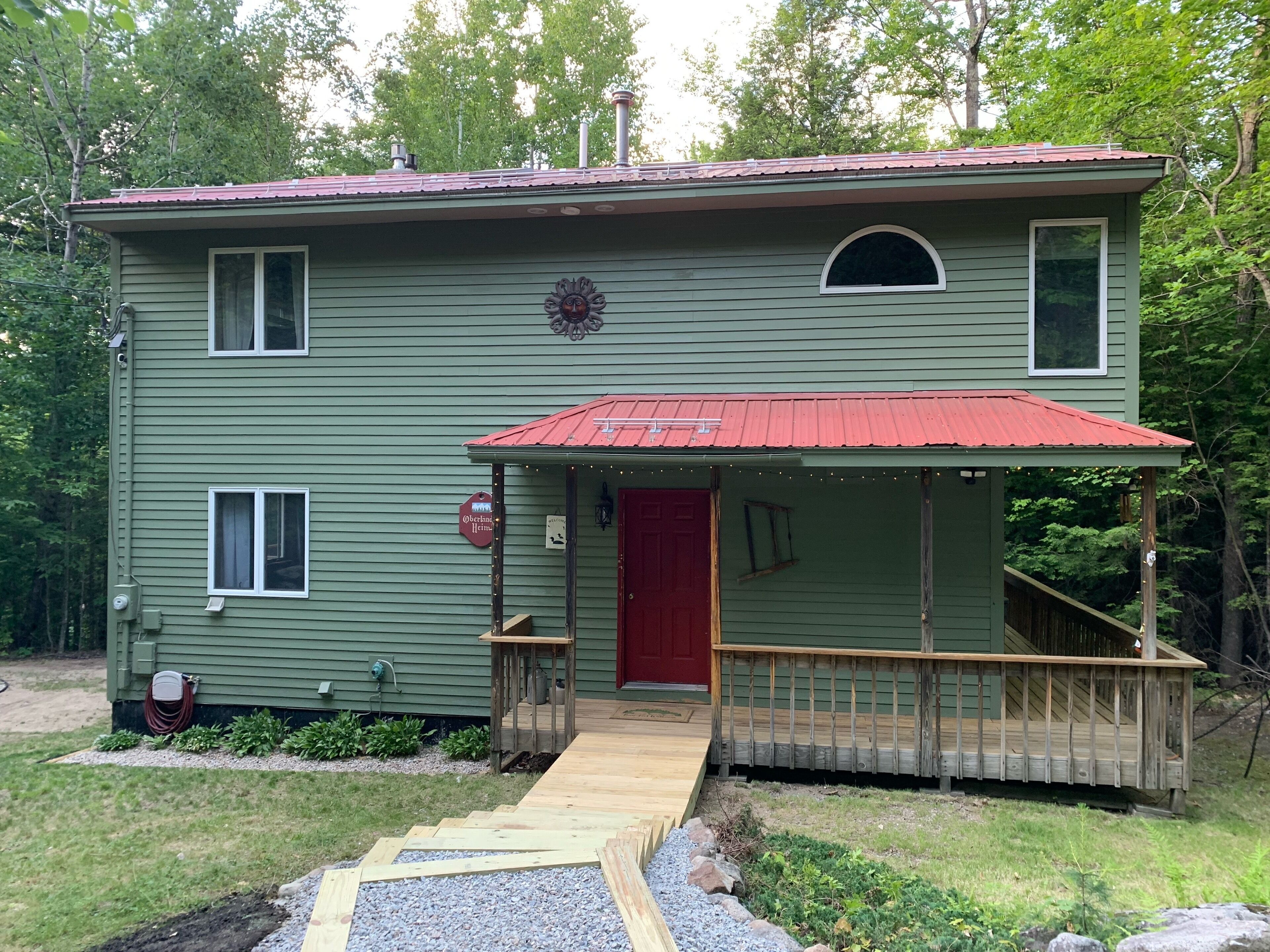 Une maison à deux étages avec une porte d’entrée rouge, un petit porche doté d’une balustrade en bois et un chemin de gravier menant à l’entrée.