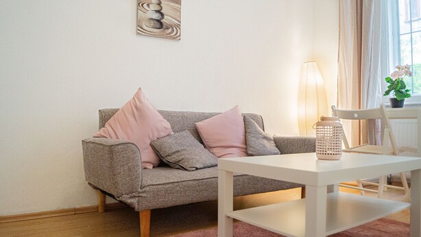 Una sala de estar con un sofá gris, una mesa de centro blanca y una lámpara.