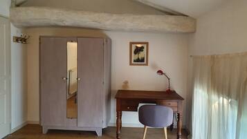 Una stanza con una scrivania in legno, una sedia, un armadio, un quadro appeso al muro e una finestra con tende.