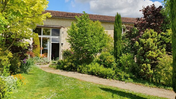 A stone house with a tiled roof, surrounded by a well-maintained garden with various plants and a gravel path. - La Prunelière, in the heart of nature (Razines)