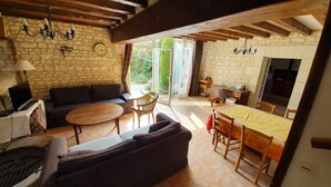 A cozy living room with a stone wall, wooden beams, a sofa, a coffee table, and a dining area with a table and chairs. - La Prunelière, in the heart of nature (Razines)