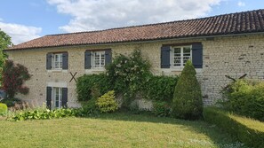 A stone building with a tiled roof, three windows with shutters, and a well-maintained garden with grass and shrubs. - La Prunelière, in the heart of nature (Razines)