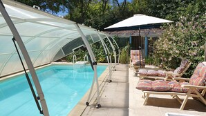 A swimming pool with a glass enclosure, surrounded by lounge chairs and a covered seating area. - La Prunelière, in the heart of nature (Razines)