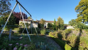 A garden with a swing set, a stone house, and a clear blue sky. - La Prunelière, in the heart of nature (Razines)