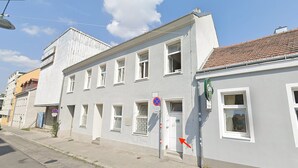 A two-story building with a white facade and a red-tiled roof. There are multiple windows, some with bars, and a no parking sign is visible. - Shared Modern Apartment Schönbrunn - Budget Chic Room (Vienna)