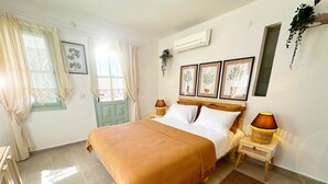 A neatly arranged bedroom with a bed, two bedside tables, a window with curtains, and a wall-mounted air conditioner. - Monk Island Guesthouse (Foça)