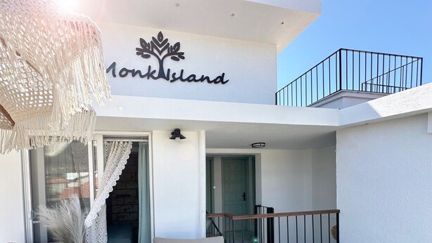 A balcony with two cushioned chairs, a woven vase, and a chandelier. - Monk Island Guesthouse (Foça)