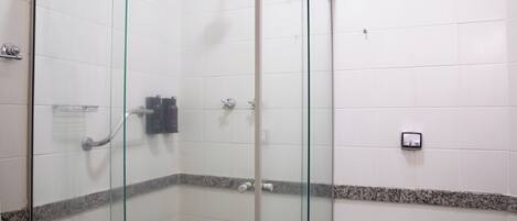Un vestuario de ducha con paredes de vidrio, un cabezal de ducha manual, un perchero y un dispensador de jabón en la pared.