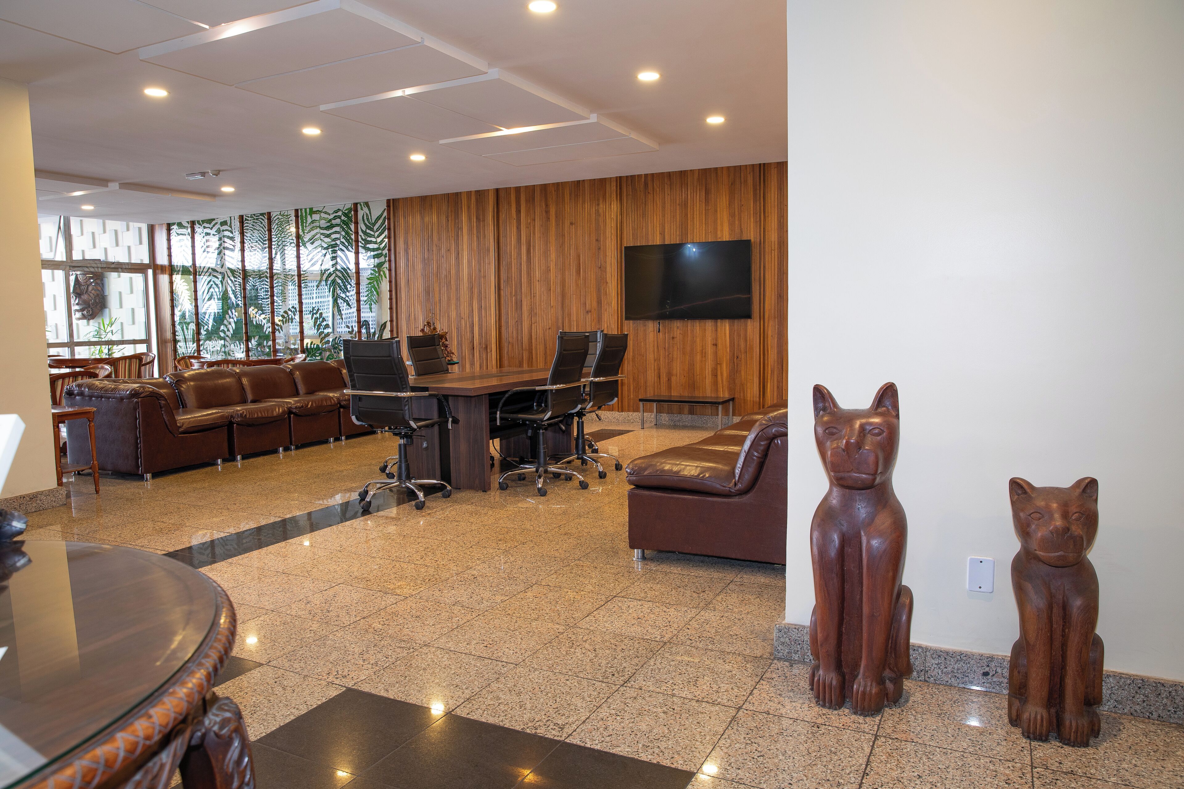 A modern meeting room with a wooden panel wall, a large flat-screen TV, and a conference table surrounded by chairs.