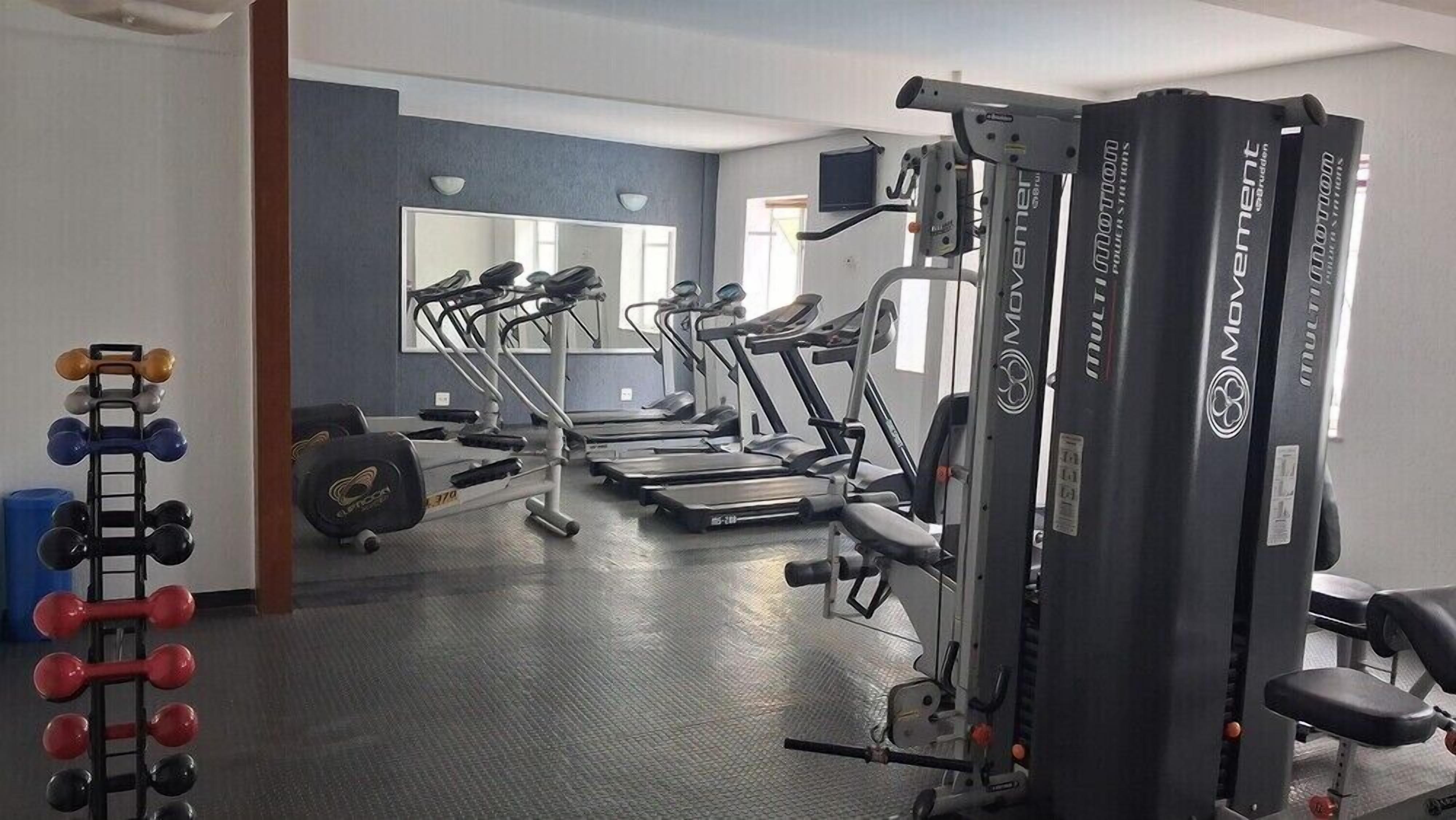 Une salle de sport équipée de tapis de course, d’appareils de musculation et d’haltères.