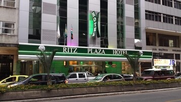 Um Hotel Ritz Plaza com fachada moderna, várias bandeiras e entrada verde.