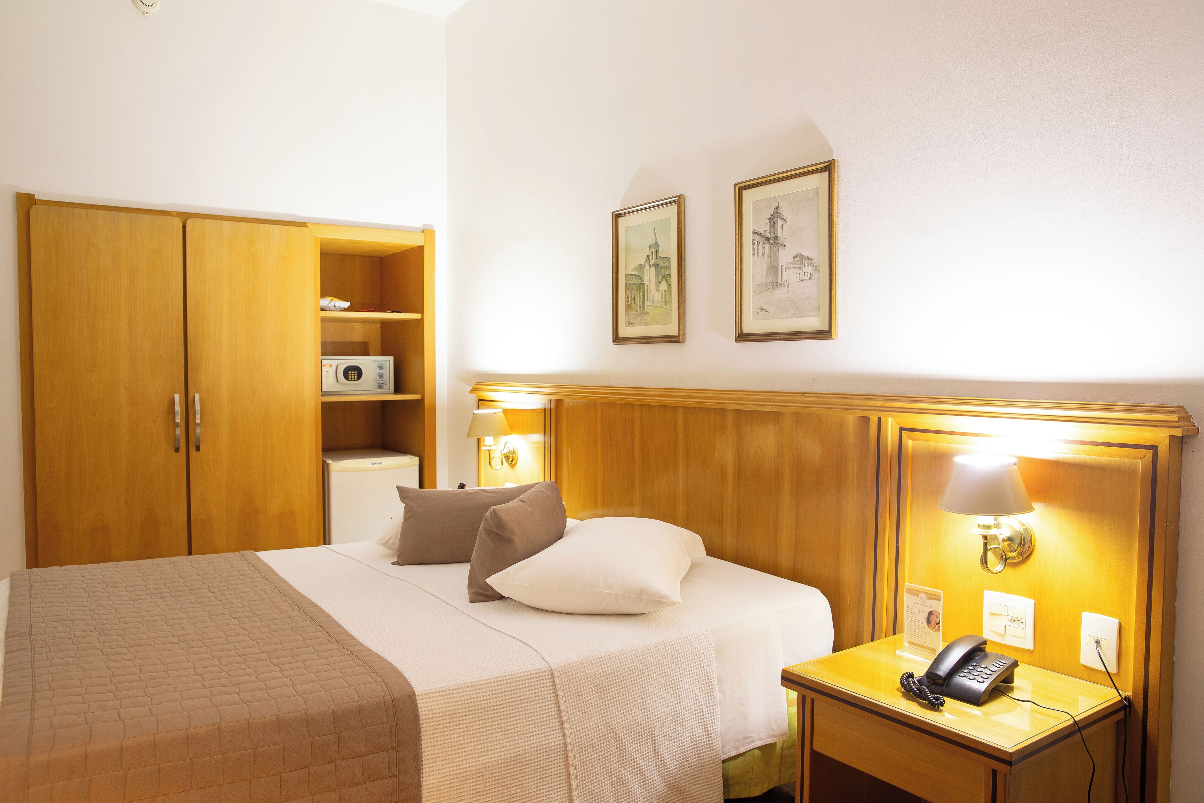 A hotel room with a bed, bedside lamp, nightstand, and a wooden wardrobe.