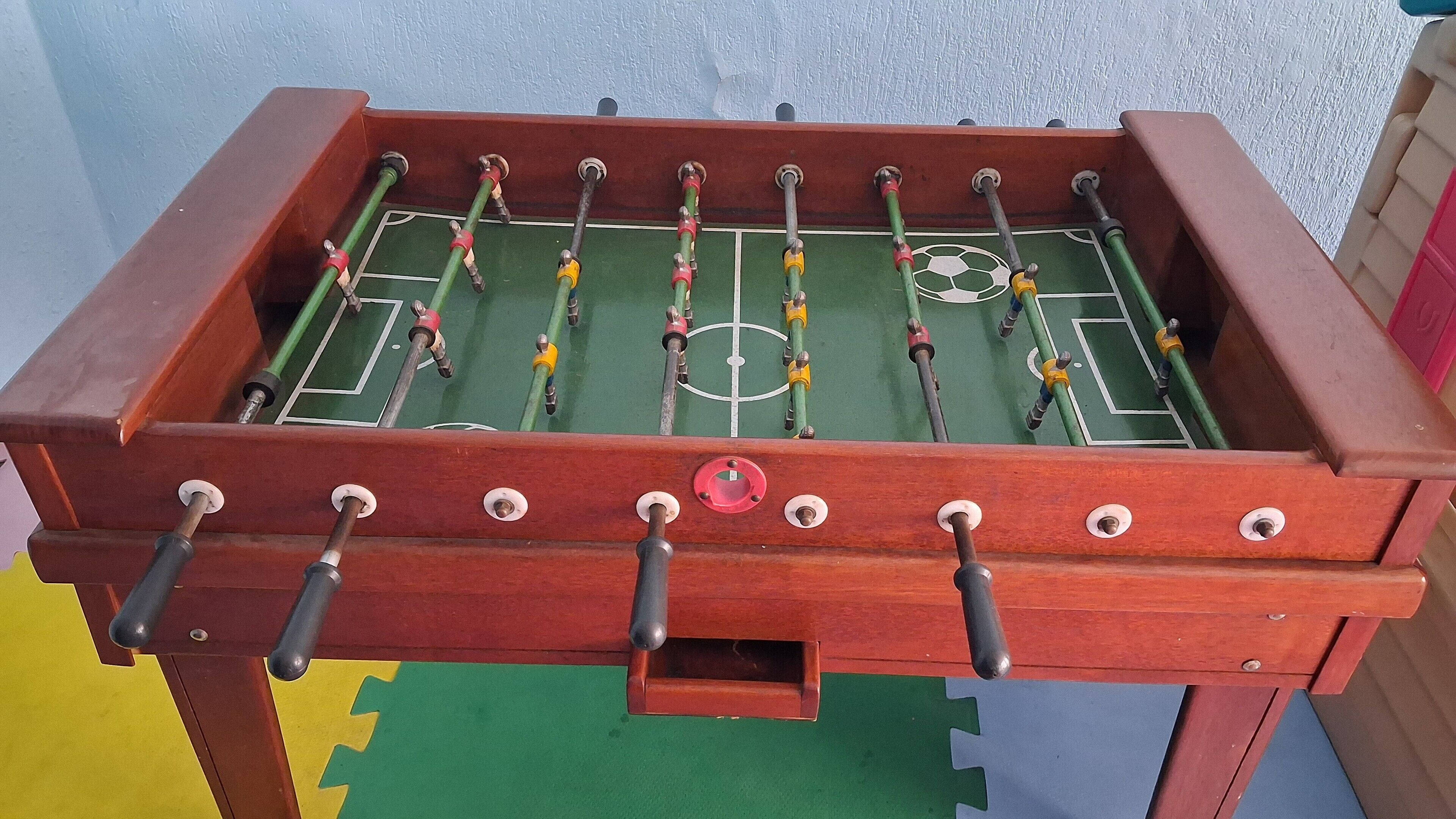 A wooden foosball table with a soccer field layout, including goal areas and a central circle.