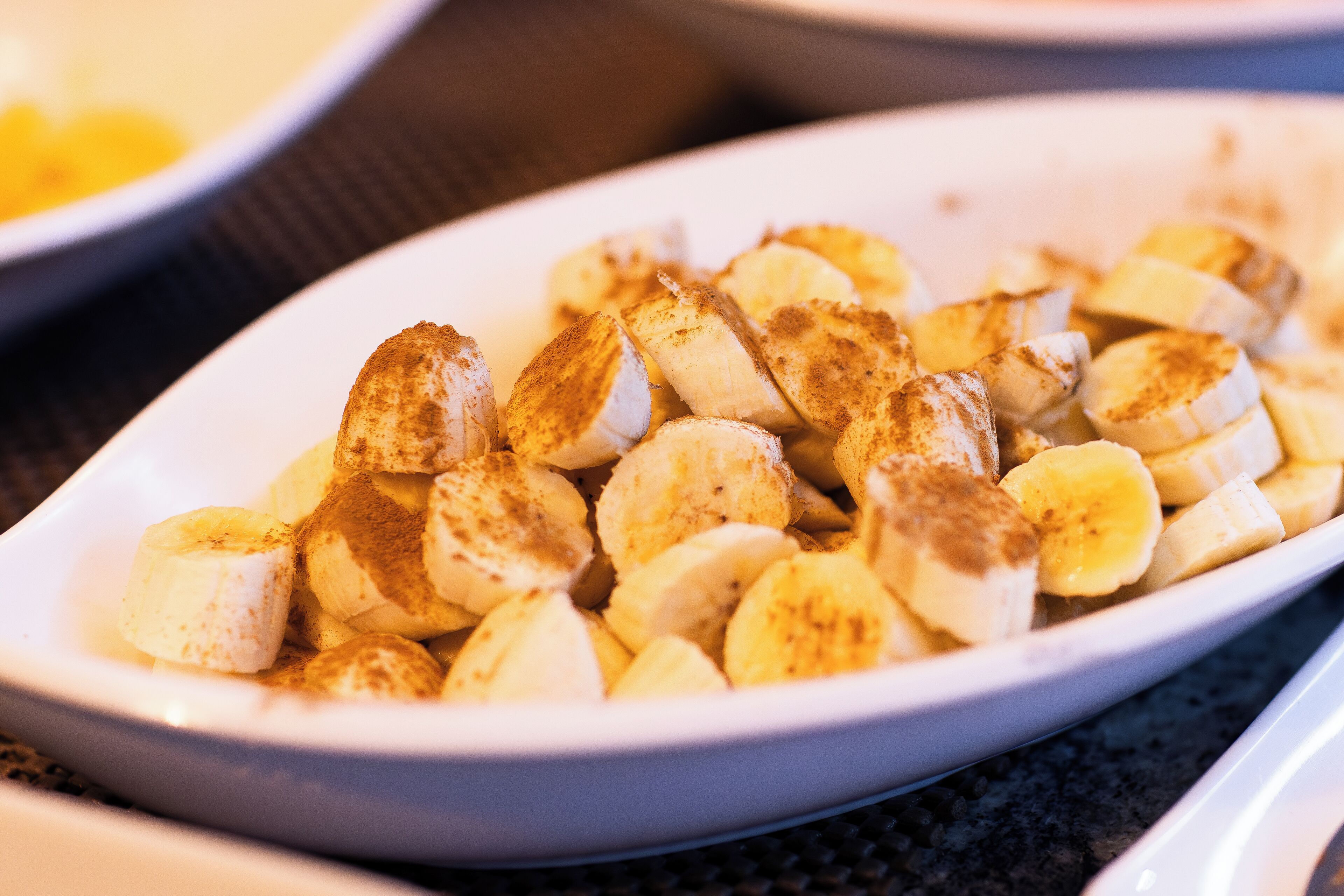 Une assiette ovale blanche remplie de rondelles de bananes saupoudrées de cannelle.