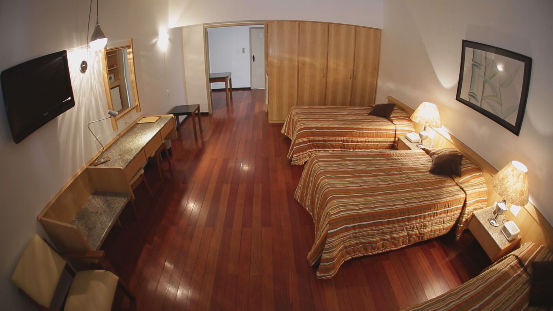 A hotel room with two beds, a desk, a chair, a TV, and a wardrobe.