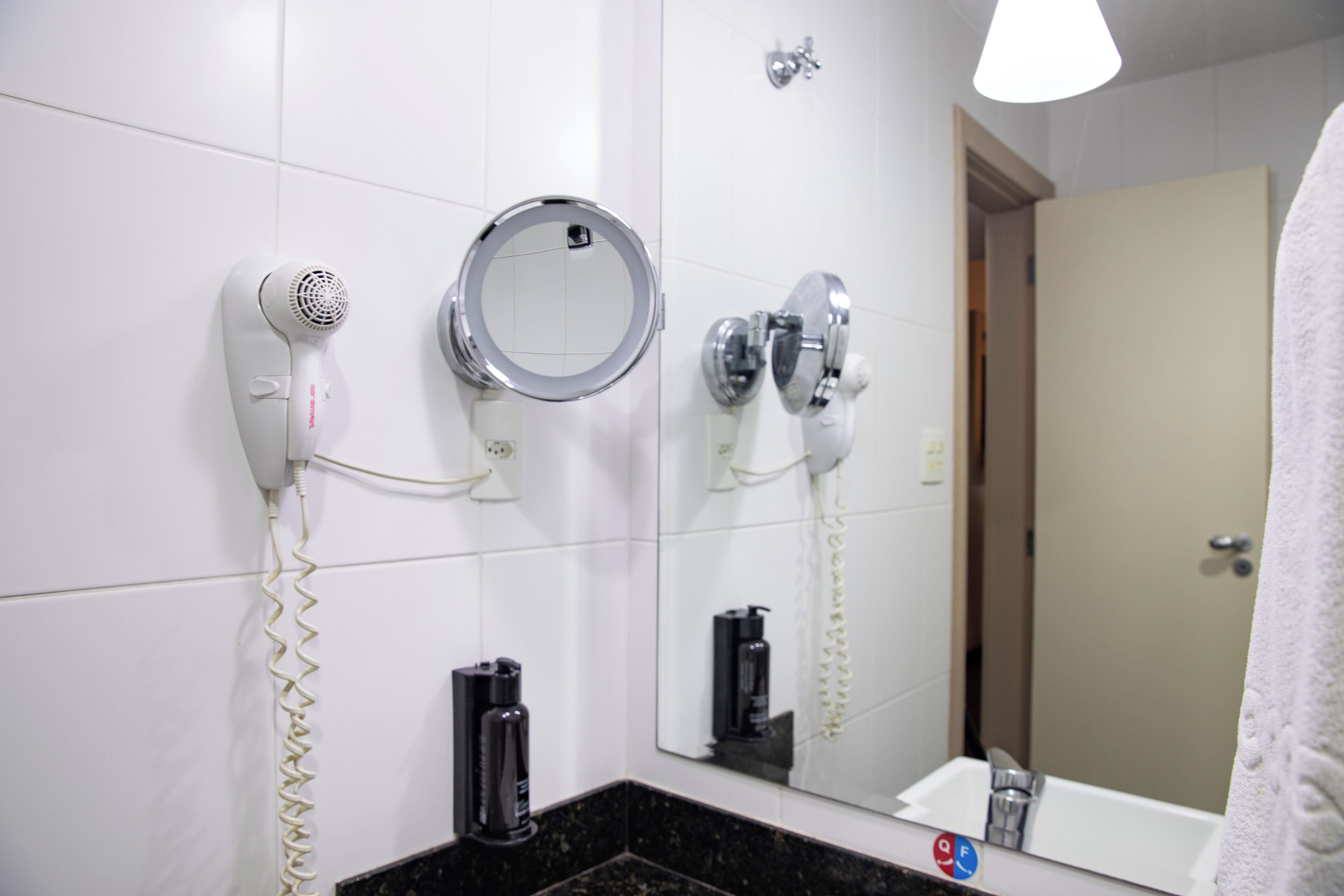 A bathroom with a hairdryer, a round mirror, a towel rack, and a sink.