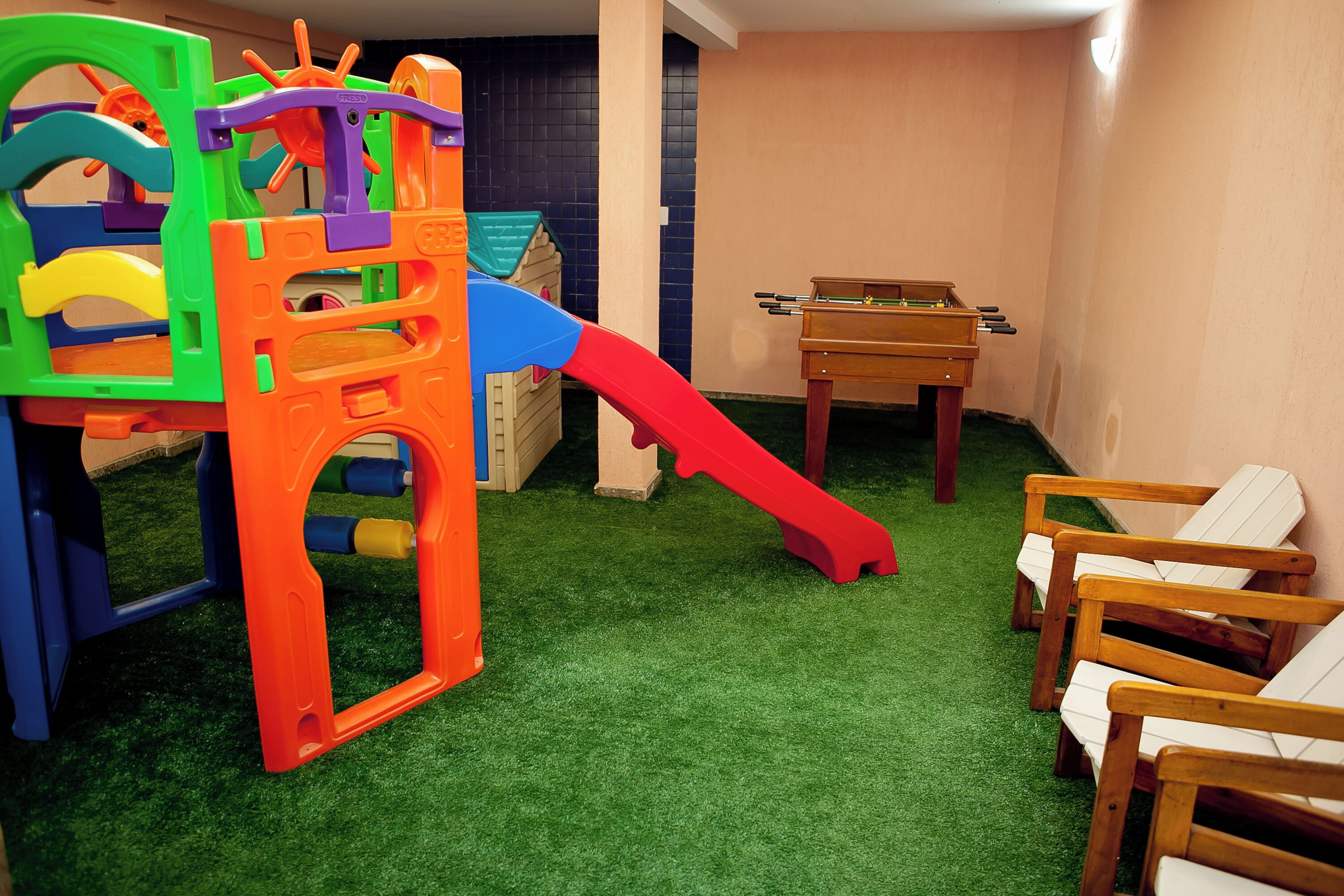 A children's play area with a colorful play structure, a red slide, and a foosball table.