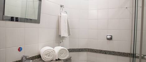 Un baño con lavamanos, espejo, toallero y ducha.