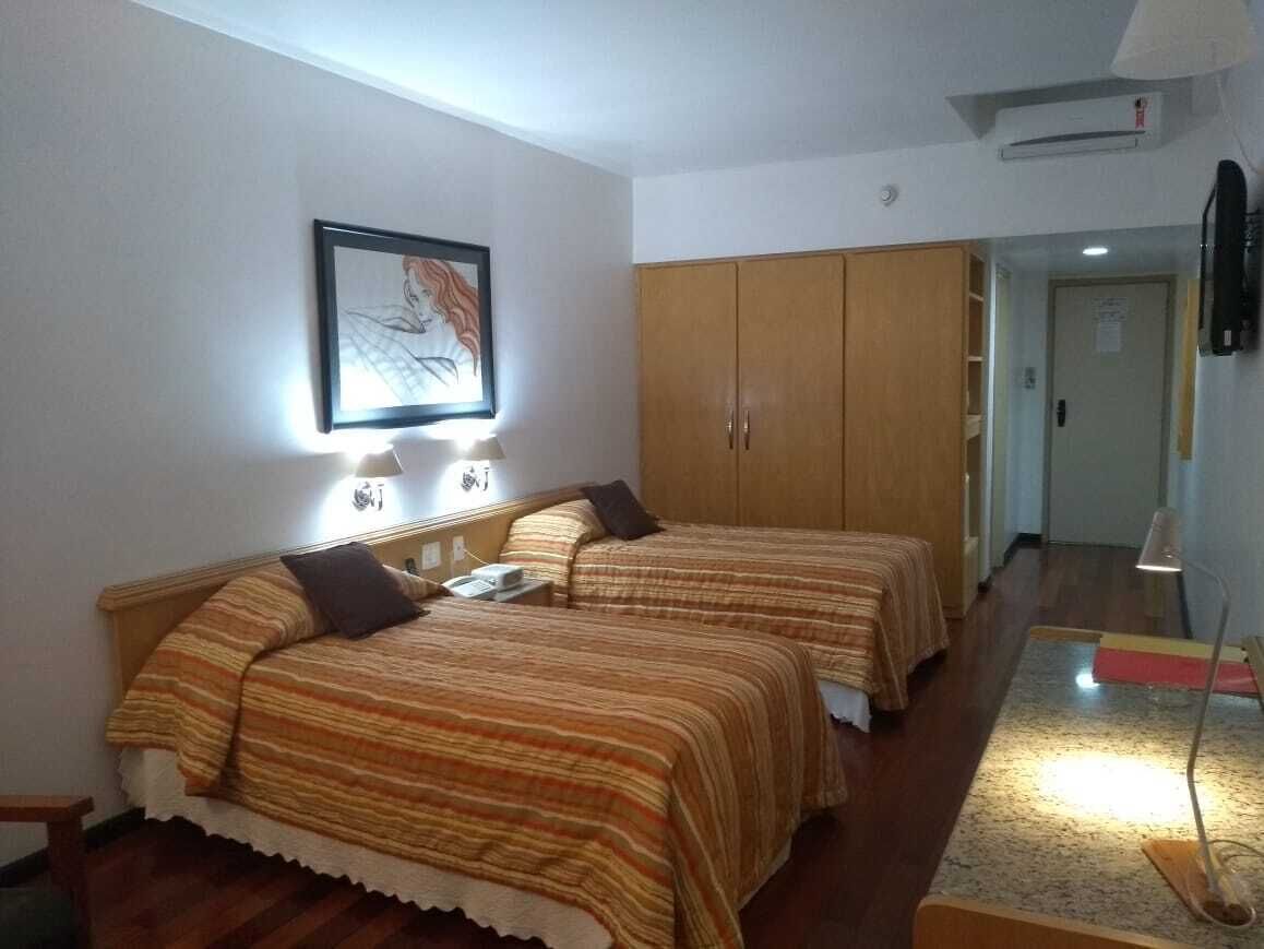 A bedroom with two beds, a wardrobe, a TV, and a desk with a lamp.