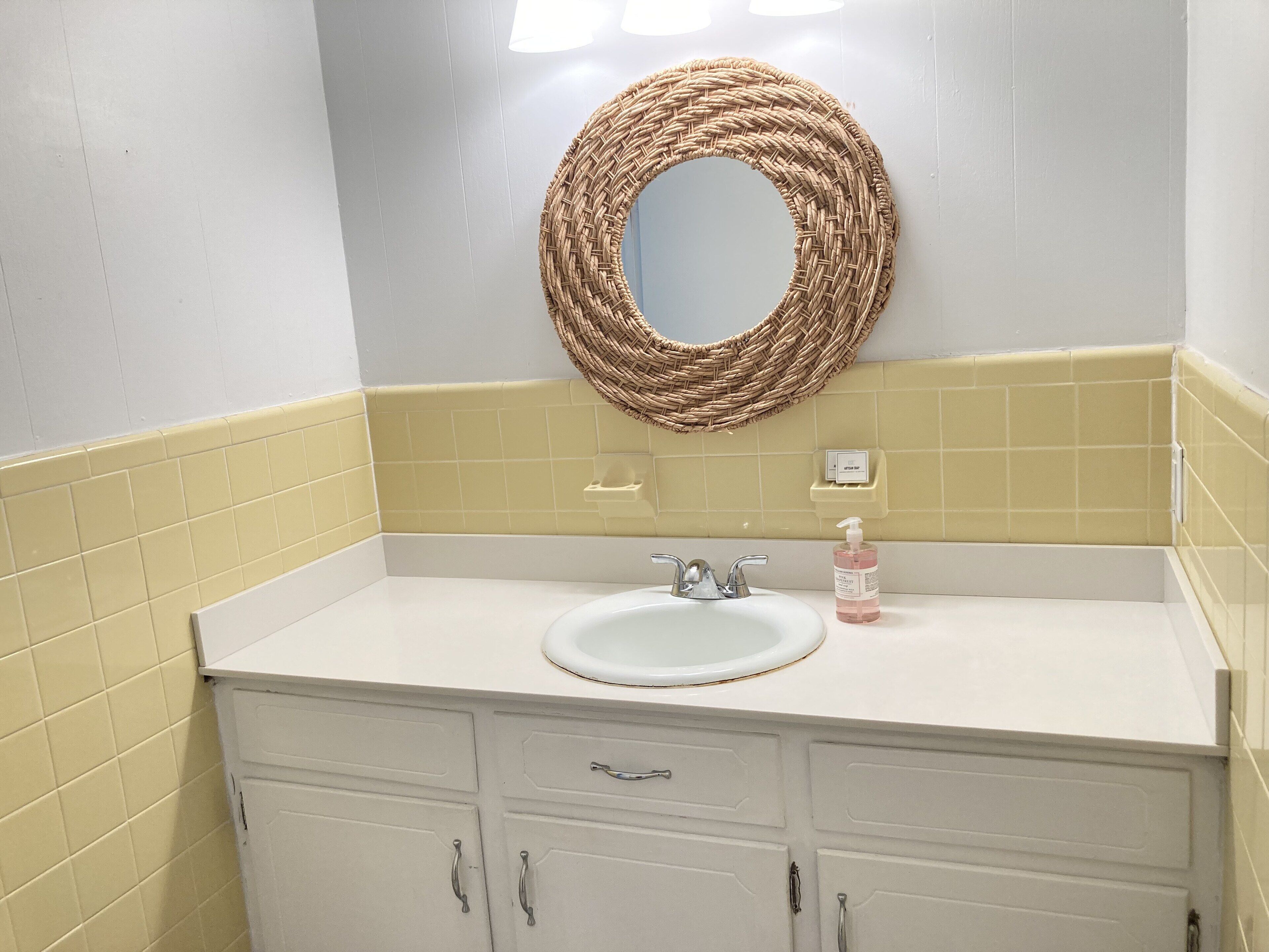 Ein Badezimmer mit einem weißen Waschbecken, einem Spiegel und einer Seifenspender.