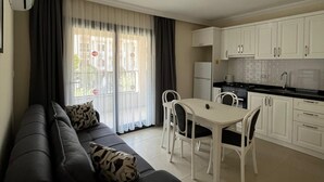 Una sala de estar moderna con un sofá oscuro, una mesa de comedor y armarios blancos.