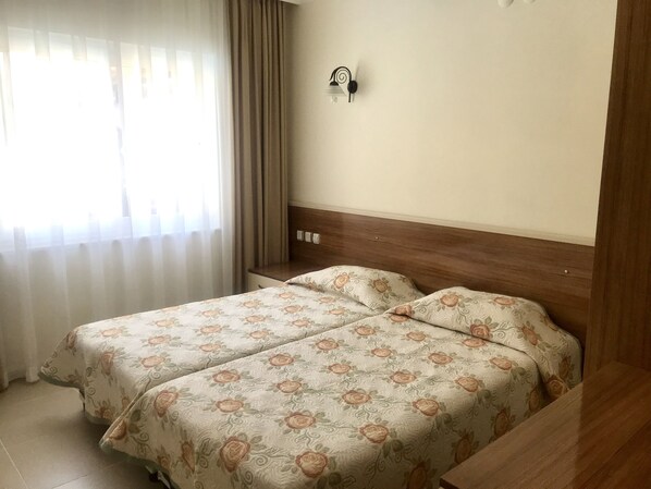 Hotellihuone, jossa on kaksi sänkyä, puinen pääty, yöpöytä ja seinään kiinnitetty valaisin.