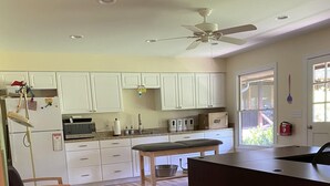 A kitchen with white cabinets, a wooden dining table, and a ceiling fan. - The Pill Box is the perfect getaway next to the Cowpasture River (Millboro Springs)
