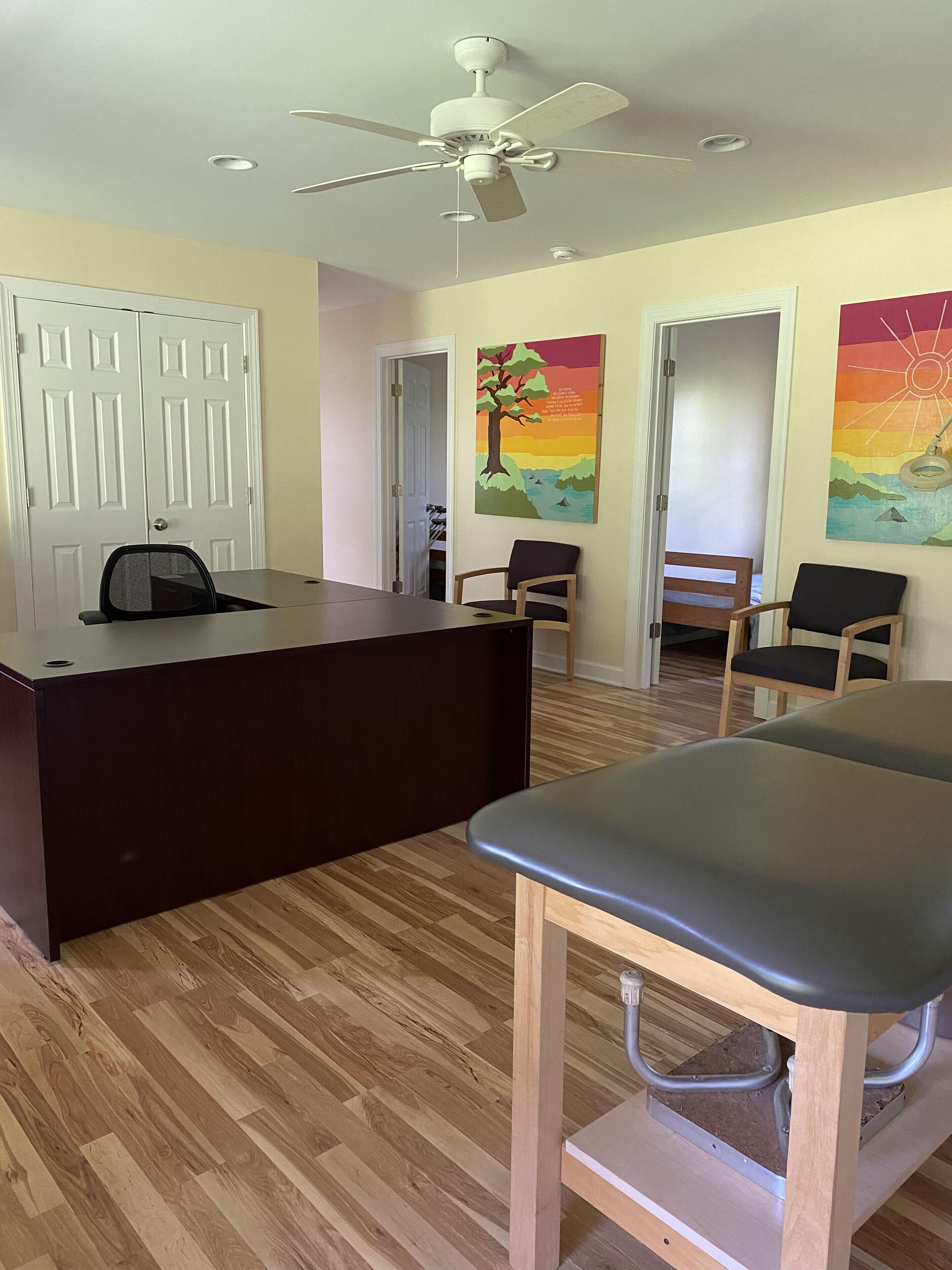A reception area with a desk, chairs, a ceiling fan, and artwork on the walls.