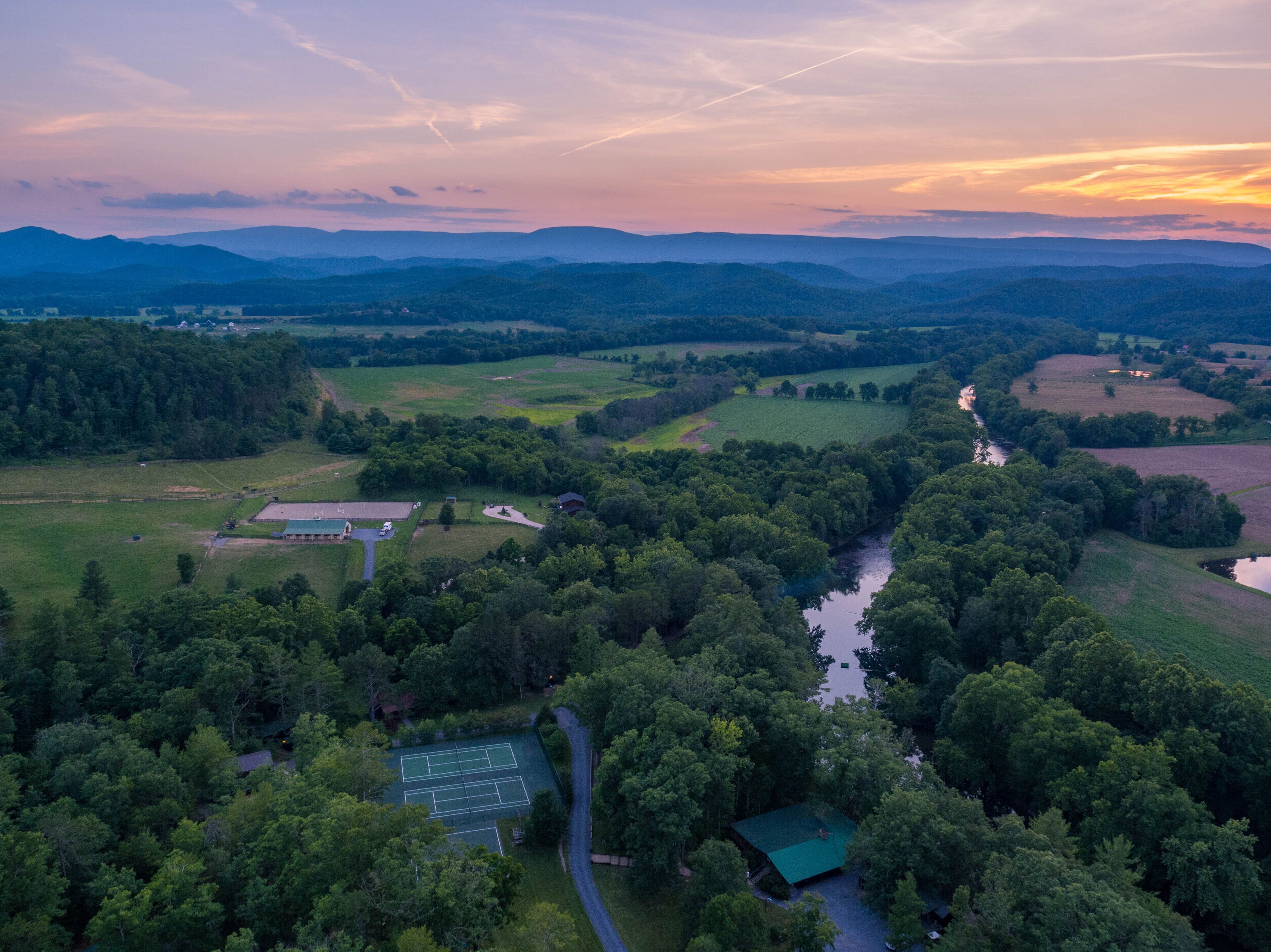 An aerial view of a rural landscape with a tennis court, a small building, and a river.