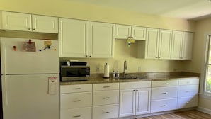 A kitchen with white cabinets, a refrigerator, a microwave, a sink, and wooden flooring. - The Pill Box is the perfect getaway next to the Cowpasture River (Millboro Springs)